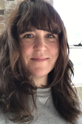 A photograph of Clare Britton. She is a young adult white woman, with shoulder-length brown hair. She smiles.