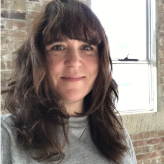 A photograph of Clare Britton. She is a young adult white woman, with shoulder-length brown hair. She smiles.