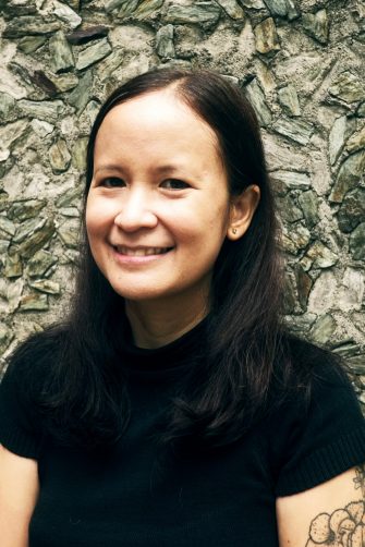 Conchitina Cruz, a Phillipina woman with shoulder-length dark hair. She smiles. On her left bicep is a floral tattoo.