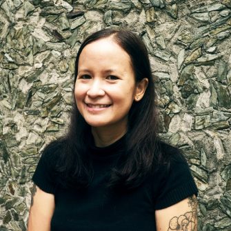 Conchitina Cruz, a Phillipina woman with shoulder-length dark hair. She smiles. On her left bicep is a floral tattoo.