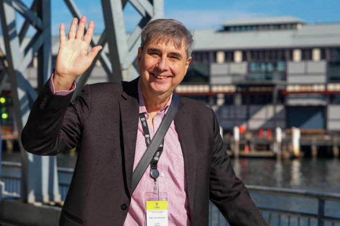 Man smiling and waving at camera by the harbour